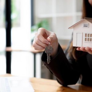 attractive-young-female-house-realtor-or-real-estate-agent-holding-house-keys-chain-and-house-model-blurred-background-free-photo